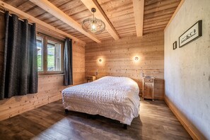 Ein Zimmer aus Holz mit einem Bett, zwei Nachttischen, einem Fenster mit Vorhängen und einer Wandleuchte.