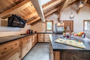 Une cuisine avec des armoires en bois, un plan de travail noir, une cuisinière encastrée et un luminaire suspendu.