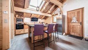 A kitchen with wooden beams, a central island with purple chairs, a microwave, a stove, and a refrigerator.
