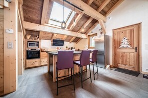 Une cuisine avec des poutres en bois, un îlot central avec des chaises violettes, un four à micro-ondes, une cuisinière et un réfrigérateur.
