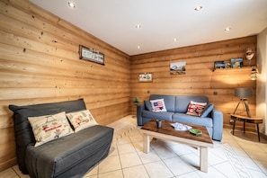 A cozy room with a dark grey sofa, a blue sofa with decorative pillows, a wooden coffee table, and a lamp on a wooden side table. - Apartment 'Appartement Chalet - Le Vnipi' with Mountain View, Balcony and Wi-Fi (Abondance)