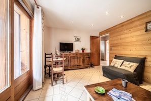 Un soggiorno con divano, tavolino, televisore, mobili contenitori in legno e un'area pranzo con sedie e tavolo.