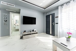 Ett modernt hotellrum med en platt-TV, ett konsolbord, en krukväxt och en dörr med texten ”HEM” på.