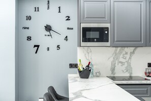 Una cocina con un reloj de pared, un microondas, un lavamanos y un protector contra salpicaduras de mármol.