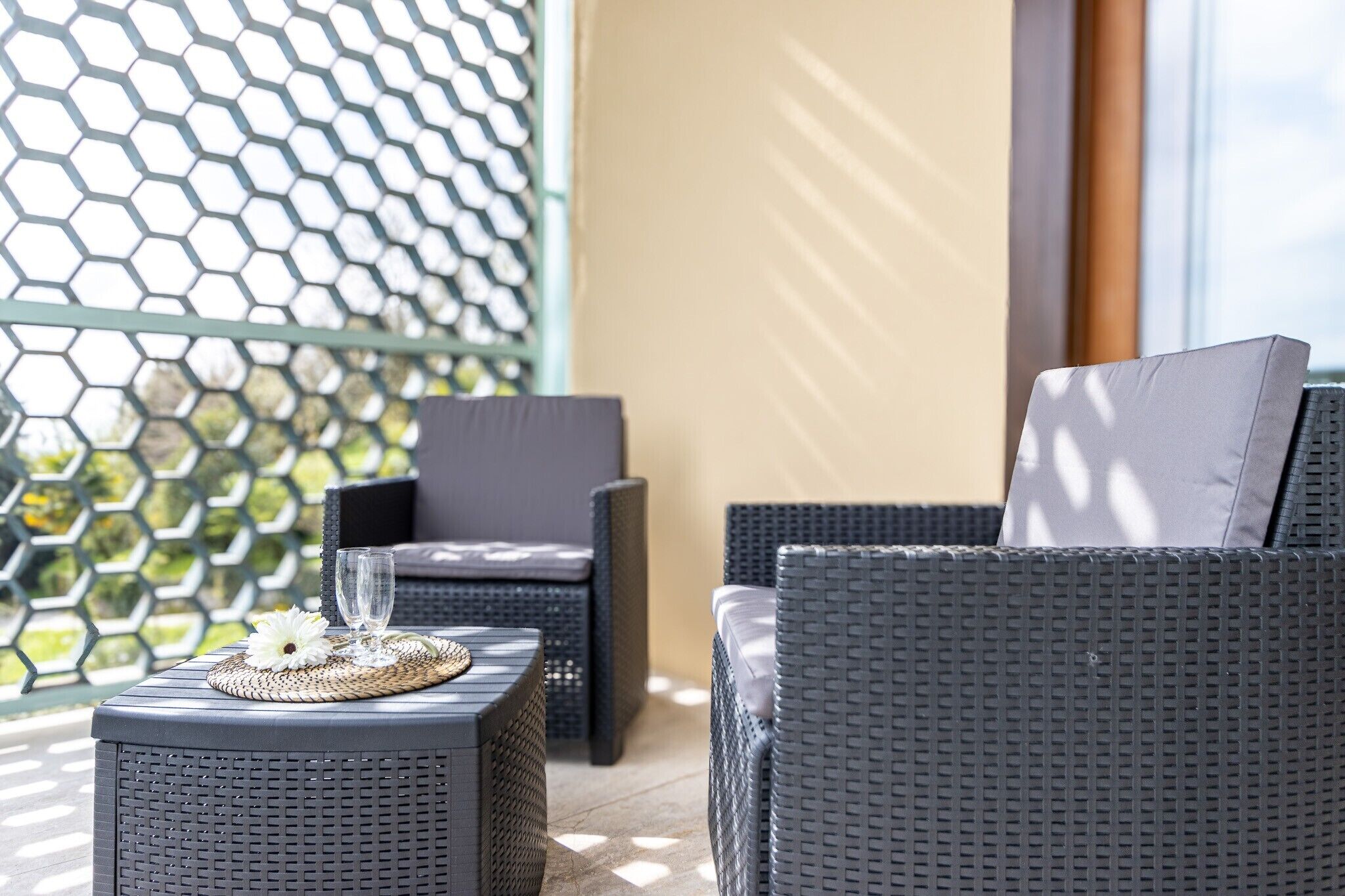 Un balcon agrémenté de meubles en osier, d’un set de table en fibres tressées et d’un verre.