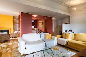 A modern living room with a white sofa, a yellow sofa, a glass coffee table, and a fireplace.