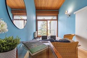 A modern room with a large mirror, a potted plant, a book, wicker furniture, and a view through large windows.