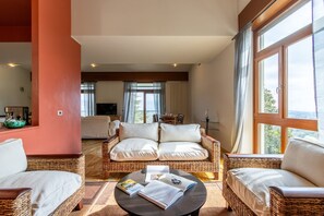 A living room with a sofa, two armchairs, a coffee table with books, and a TV.