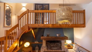 Un espacio habitable tipo loft con una escalera de madera, una chimenea, una lámpara colgante y una zona de estar acogedora.