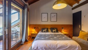 Un dormitorio con una cama grande, dos mesitas de noche, un sofá, un ventanal corredero y techo de madera.