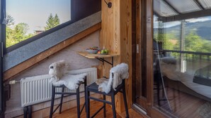 Una habitación con techo de madera, una ventana que da a árboles, un radiador y dos sillas.