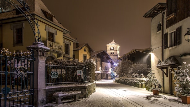 Een besneeuwde straat met gebouwen, een poort en een toren in de verte.