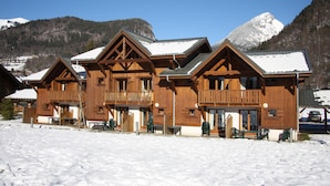 Een houten lodge met balkons, een met sneeuw bedekte grond en bergen op de achtergrond.