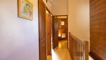 Un couloir avec des portes en bois, une carte encadrée et une lampe visible au loin.