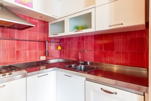 Una cocina con baldosas rojas, electrodomésticos de acero inoxidable y armarios blancos.