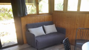 Una habitación con un sofá gris, una silla de metal y suelo de madera.
