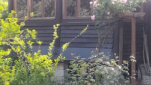 Una casa de madera con techo a dos aguas, ventanas amplias y un jardín con diversas plantas y flores.