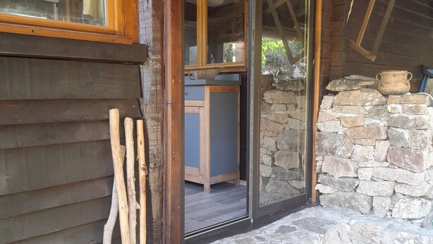 Una cabaña rústica con pared de piedra, vigas de madera y puerta de madera que da a un espacio interior.