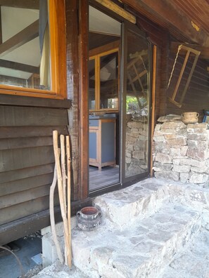 Ein rustikales Blockhaus mit Steinwand, Holzbalken und einer Holztür, die in einen Innenraum führt.
