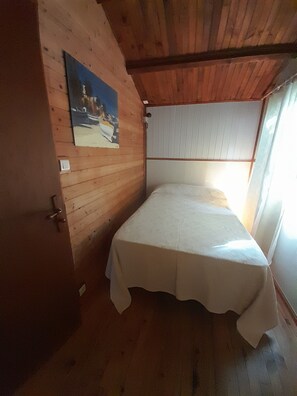 Ein kleines Zimmer mit einem Einzelbett, Holzwänden und einer schrägen Decke.