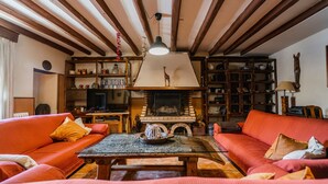 A cozy living room with a fireplace, red sofas, wooden beams, and a bookshelf. - Casa Rural 'Laguna Herrera' in Segovia – Private Pool, Garden, Sleeps up to 14 (Campo de Cuéllar)