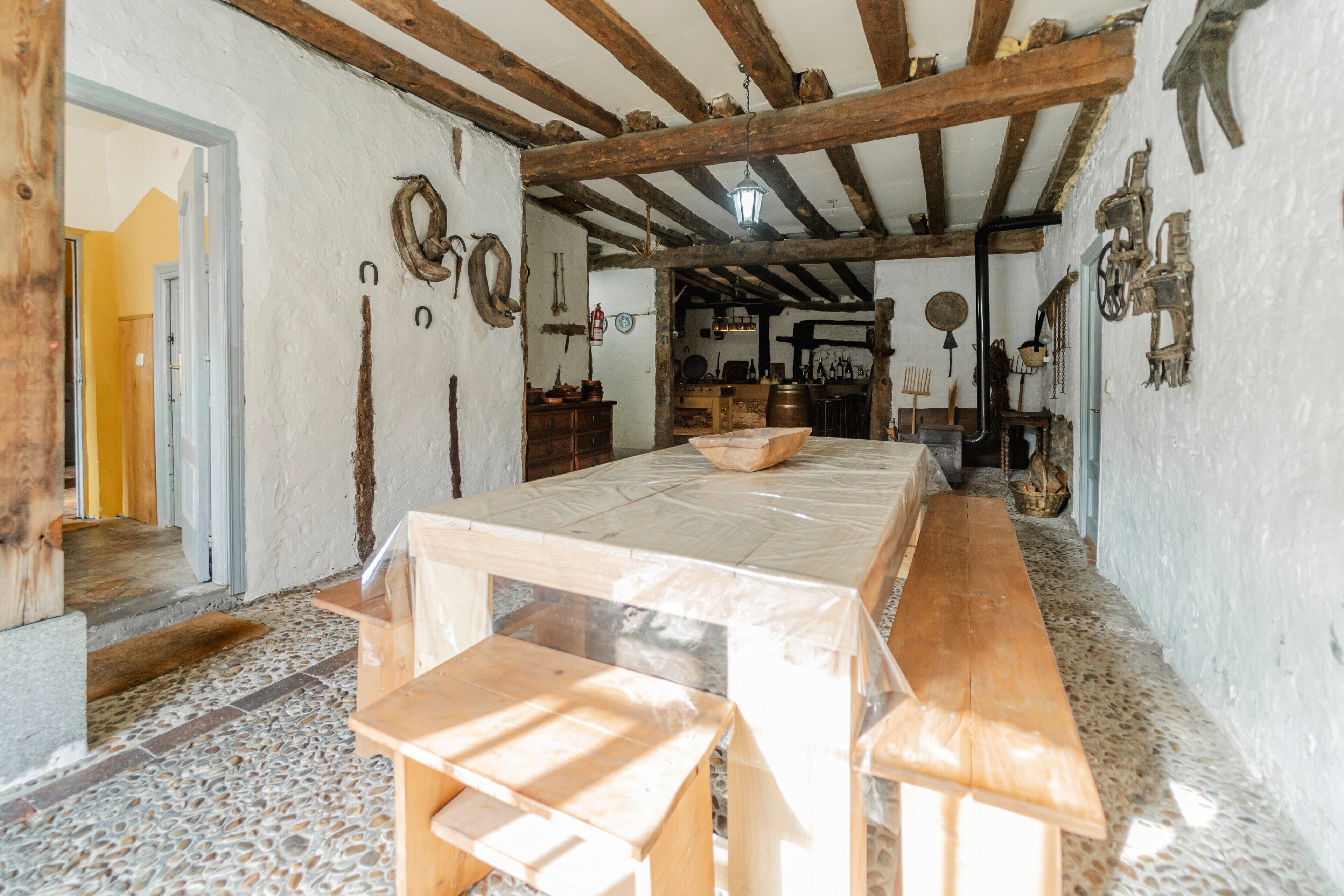 A rustic interior with a long wooden table, benches, and various tools and items on the walls.
