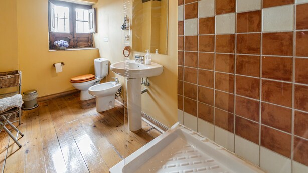 A bathroom with a wooden floor, a sink, a toilet, and a window with flowers.
