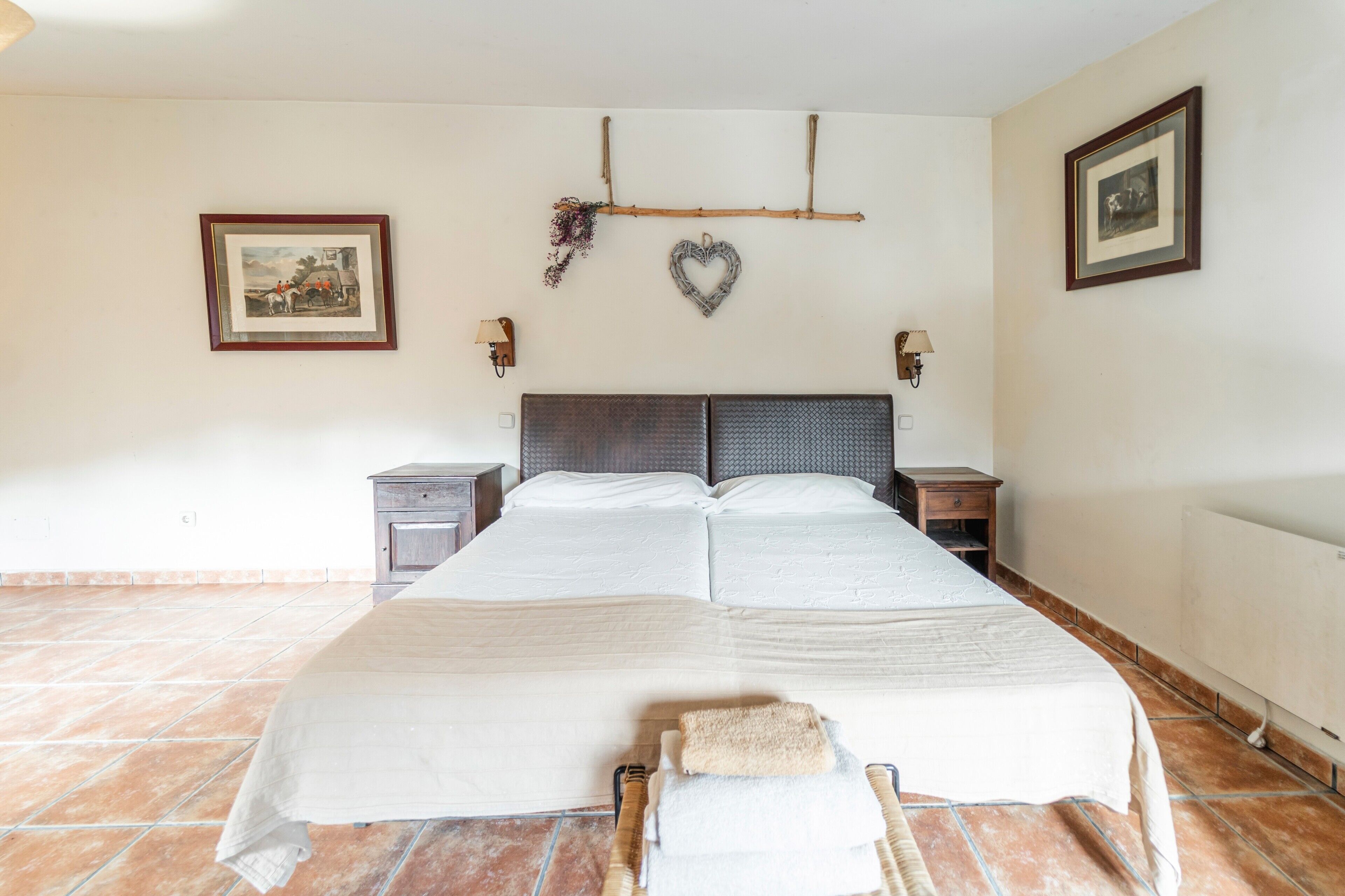 Een tweepersoonsbed met hoofdbord, twee nachtkastjes, een aan de muur bevestigd schilderij en een radiator.