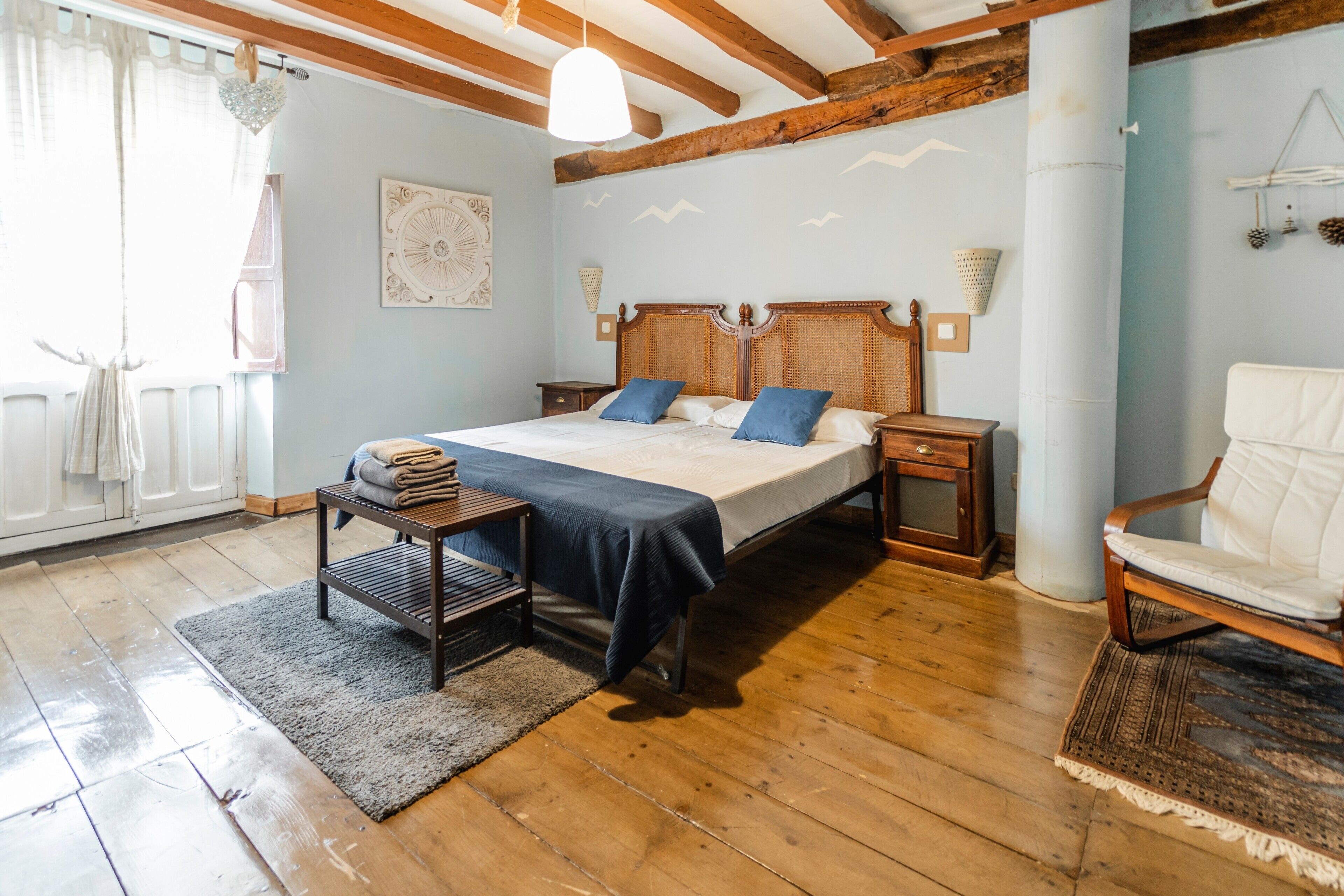 A bedroom with a wooden bed, a nightstand, a chair, and a large window.