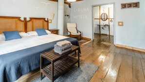 A bedroom with a large bed, a wooden bench, a chair, and a mirror. - Casa Rural 'Laguna Herrera' in Segovia – Private Pool, Garden, Sleeps up to 14 (Campo de Cuéllar)