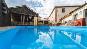 A swimming pool with a wooden fence, a wooden building with a heart-shaped decoration, and a building with a red and white facade. - Casa Rural 'Laguna Herrera' in Segovia – Private Pool, Garden, Sleeps up to 14 (Campo de Cuéllar)