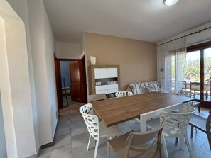 A dining area with a wooden table and white chairs, a white cabinet, and a view through a window. - Apartment 'Trilocale Centro E Mare San Teodoro' with Terrace, Garden and Air Conditioning (san teodoro)