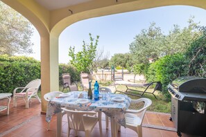 Eine Terrassengruppe im Freien mit Esstisch, Stühlen und einem Grill im Hintergrund.