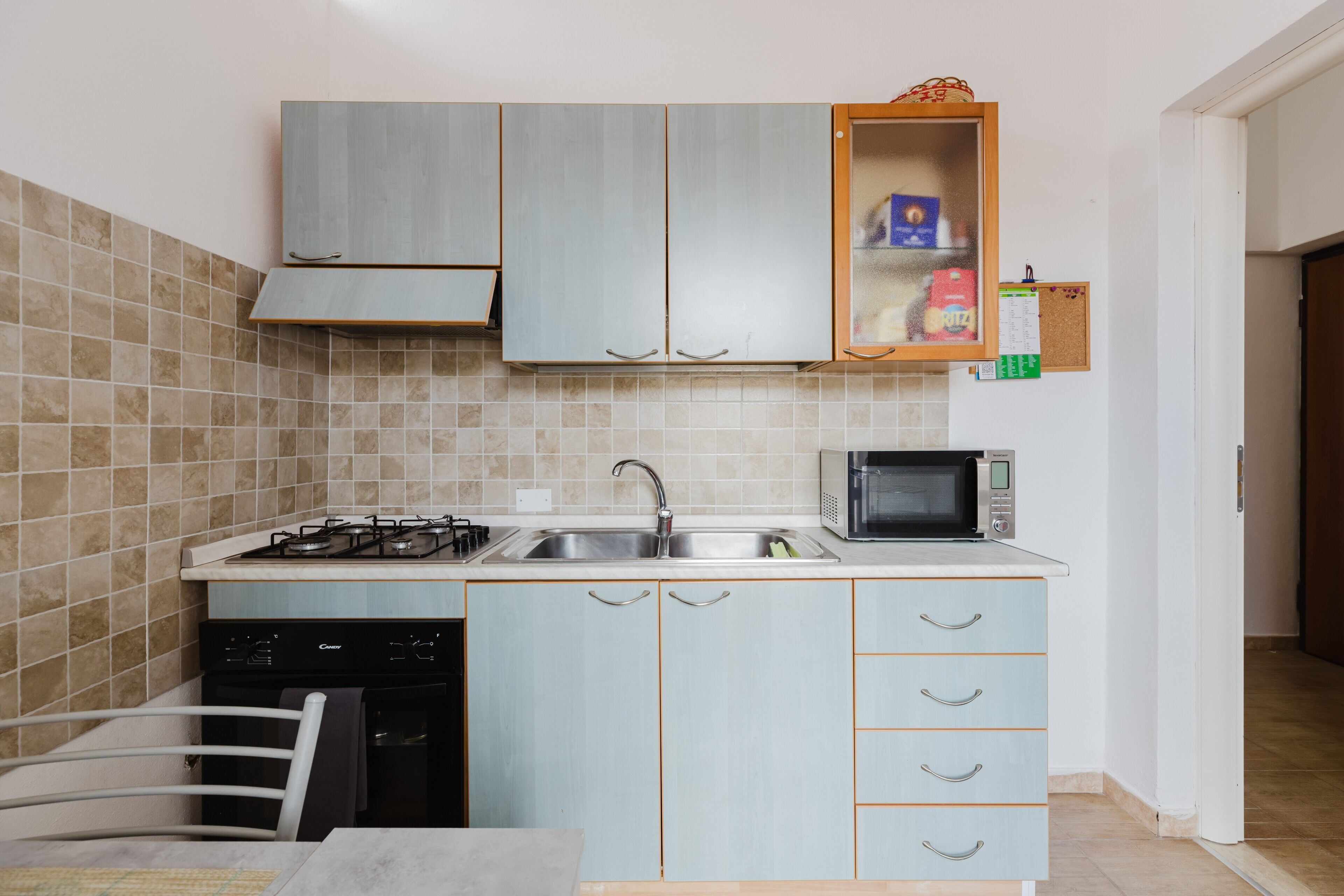 A compact kitchen with a gas stove, microwave, and a cabinet with a shelf.