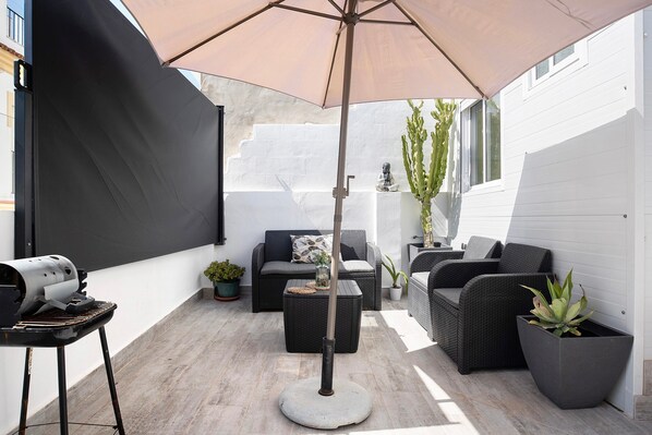 A patio with outdoor furniture, a grill, and potted plants.