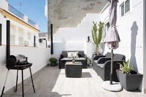 A patio with outdoor furniture, a grill, and potted plants.