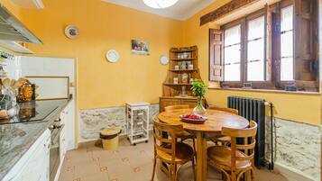 A kitchen with a dining table, chairs, a vase with flowers, a radiator, and a window with wooden shutters.