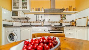 Cucina con lavatrice, forno a microonde e una ciotola di ciliegie sul tavolo.