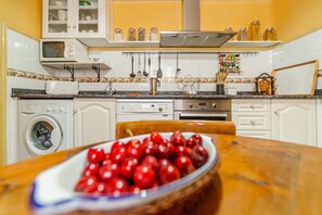 Cucina con lavatrice, forno a microonde e una ciotola di ciliegie sul tavolo.