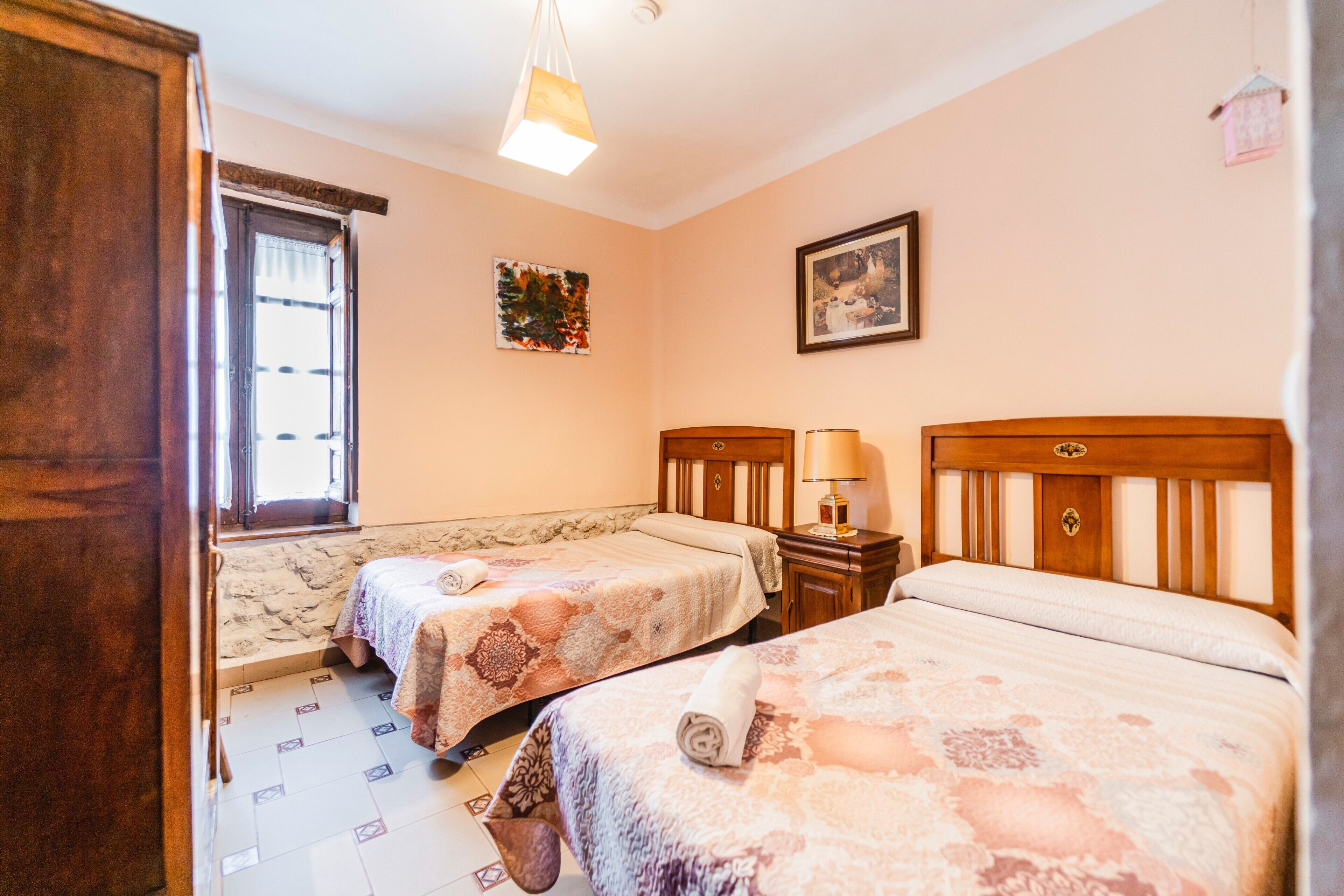 Un dormitorio con dos camas, una ventana con cortinas, un cuadro colgado en la pared y un cabecero de madera.