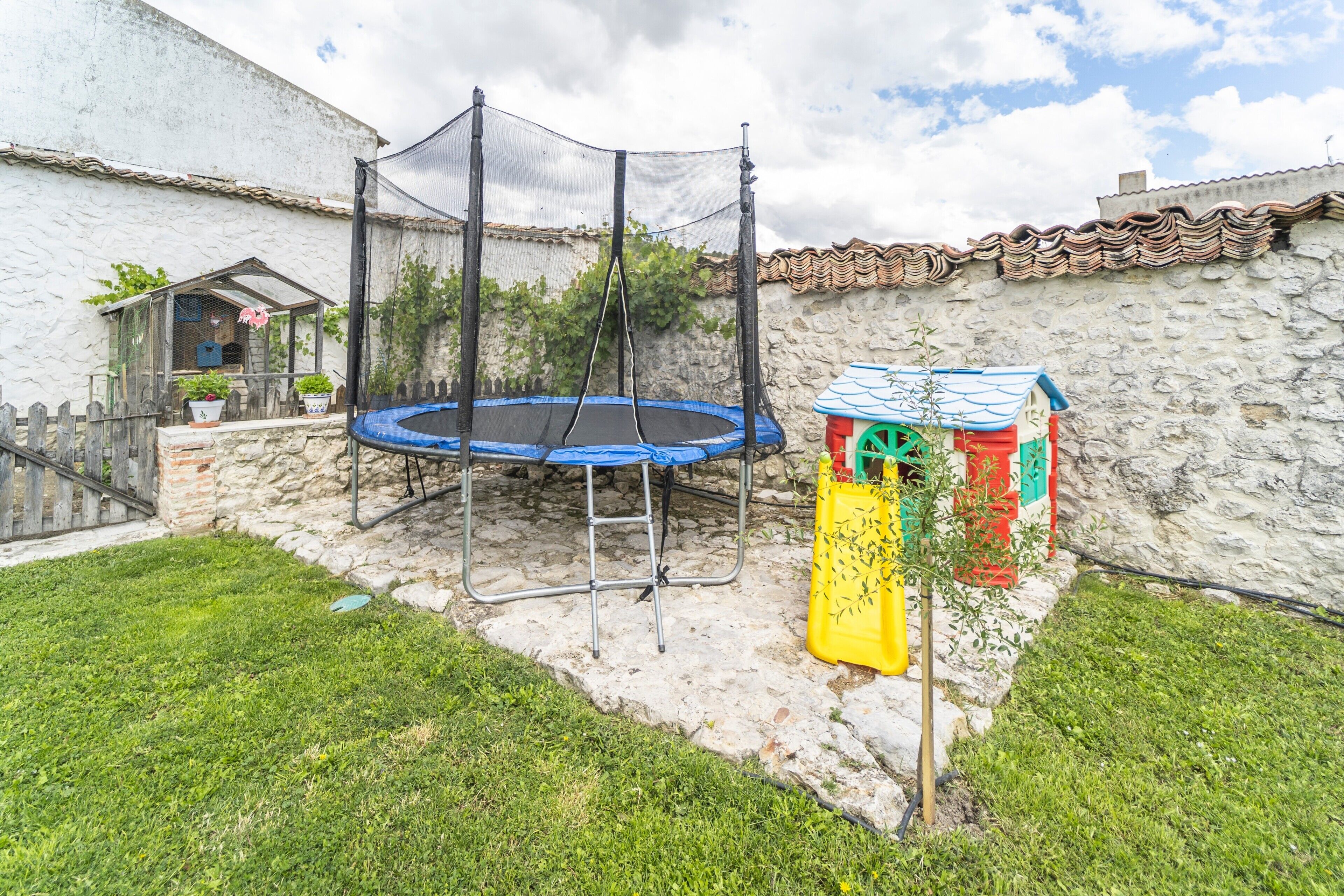 A backyard with a trampoline, a small shed, and a stone wall.
