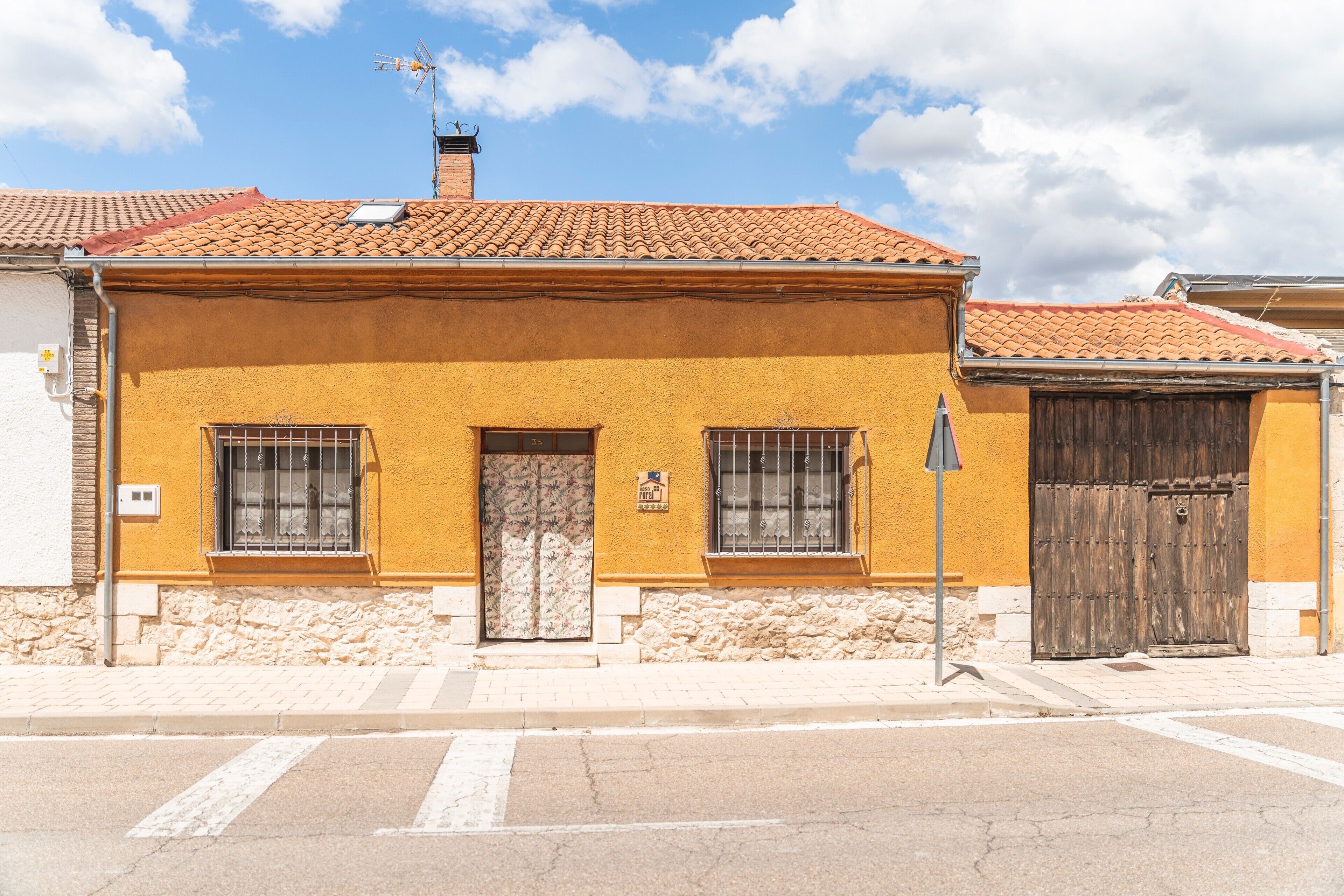 Un edificio amarillo con techo de tejas, base de piedra y puerta de madera.