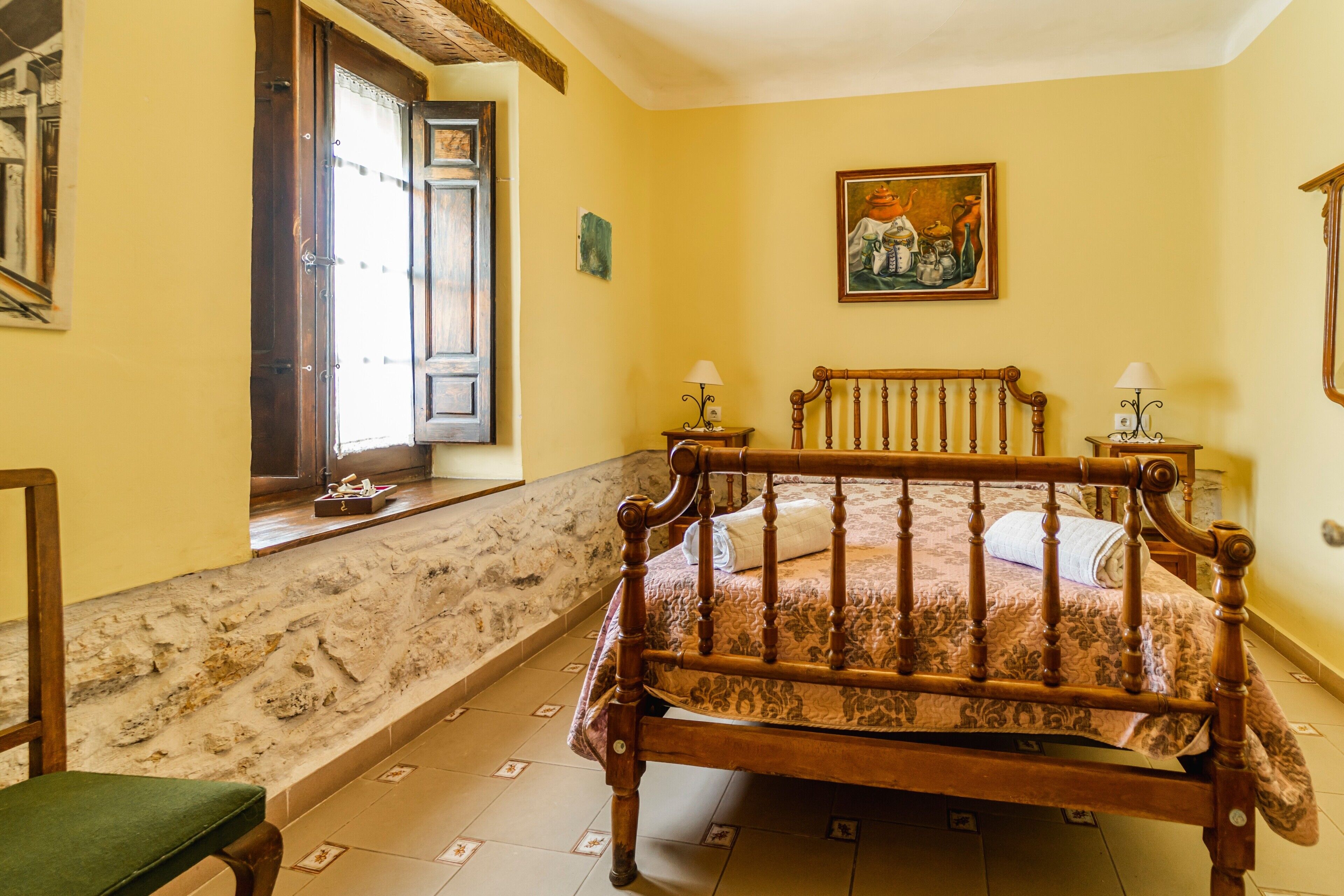 A room with a bed, a chair, a window with a view, and a painting on the wall.