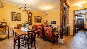 Zona pranzo con tavolo e sedie in legno, divano, lampadario, orologio e televisione.