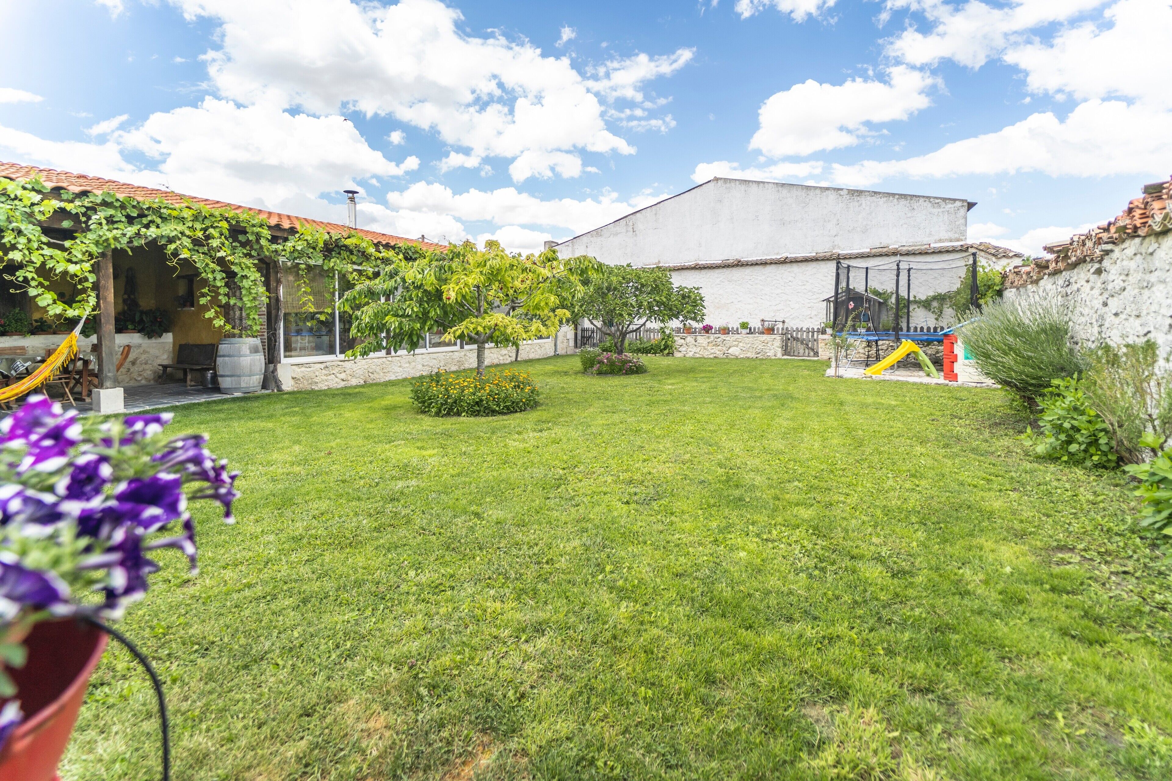 Un patio con césped, una zona de juegos y un edificio de fachada blanca.