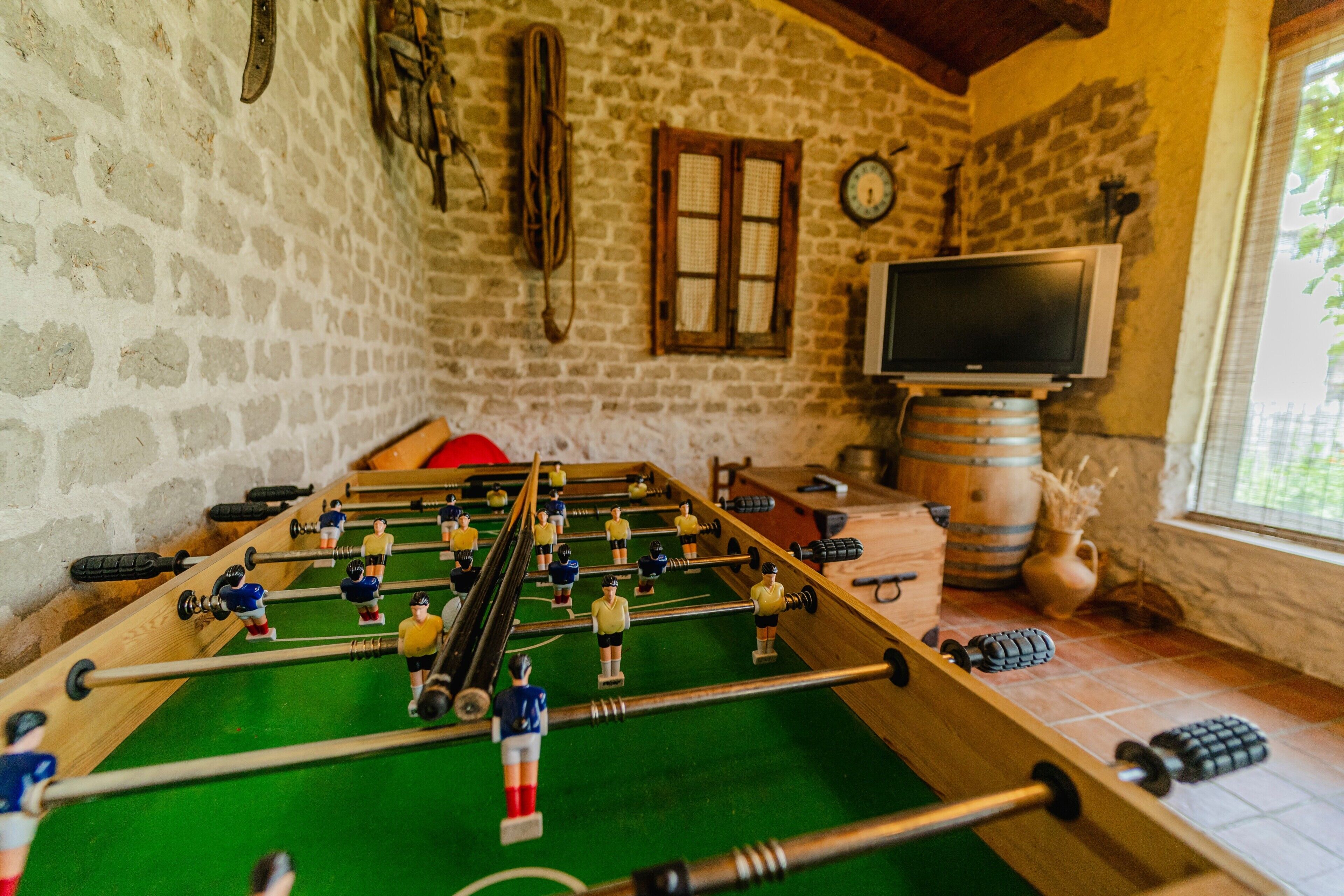 Een tafelvoetbaltafel in een ruimte met stenen muren, een televisie en een raam.