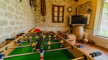 Een tafelvoetbaltafel in een ruimte met stenen muren, een televisie en een raam.
