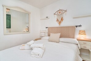 Een net opgemaakt bed met witte lakens, een bedlampje en een aan de muur hangende droomvanger.