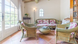 A room with wicker furniture, a round coffee table, a bookshelf, and a window with curtains. - Holiday Home 'Orangerie' with Mountain View, Shared Terrace and Wi-Fi (Bonnieux)