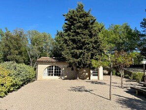 A building with a tiled roof, a gravel courtyard, and a large tree.